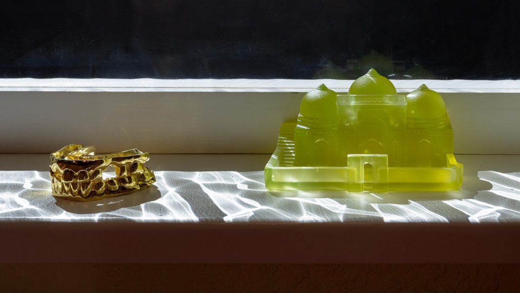 Detail of Supra (2026), installation view, Windows, If the World We, 59th Carnegie International, Carnegie Museum of Art, Pittsburgh, 2026. Photo by Zachary Riggleman_(small) Cast gold teeth beside a yellow translucent mosque model on a sunlit window sill
